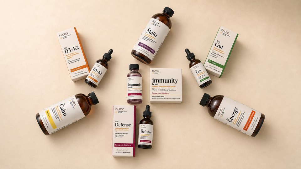 The hūma Daily Collection: seven formulas in bottles and cartons arranged on a warm ivory surface
